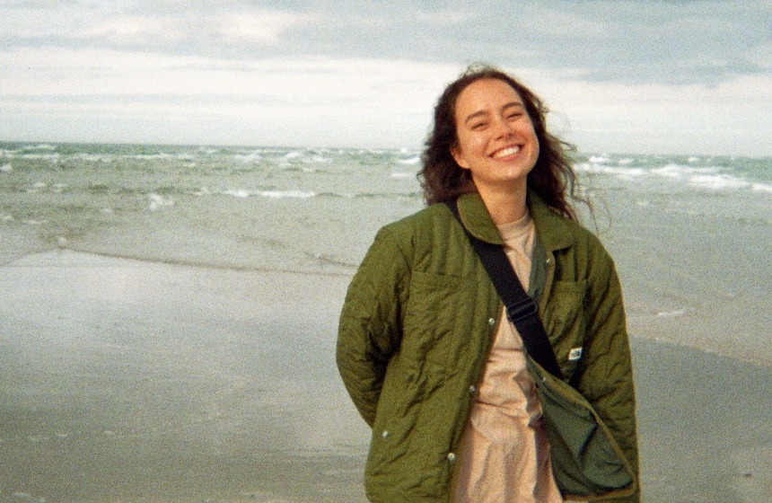 Alexandra smiling on a windy beach, wearing a green quilted jacket.